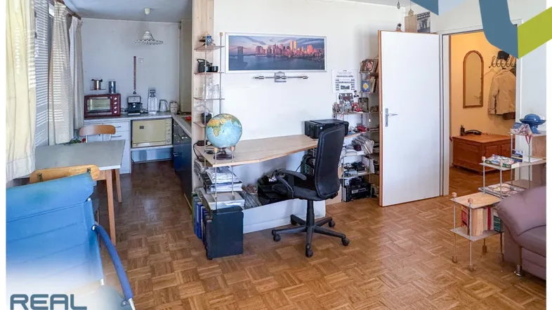Helles Wohnzimmer mit integrierter Küchenzeile, Arbeitsbereich und Parkettboden.