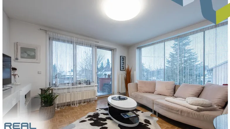 Helles Wohnzimmer mit Parkettboden, großem Sofa und Zugang zum Balkon.