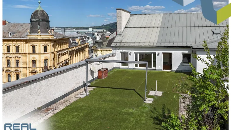 Große Dachterrasse mit Kunstrasen und weitem Blick über die Stadt und historische Gebäude.