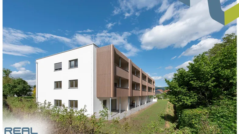 Modernes Mehrfamilienhaus mit weißer Fassade und Holzverkleidung, umgeben von grüner Landschaft.