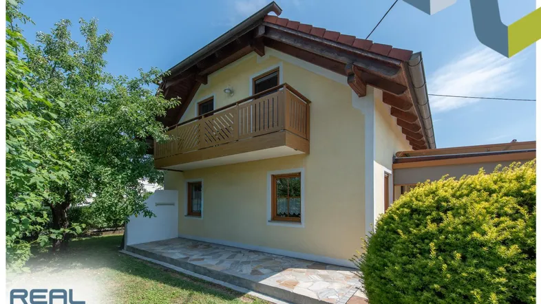 Seitlicher Blick auf das Haus mit einem charmanten Holzbalkon und einem gepflegten Gartenbereich.