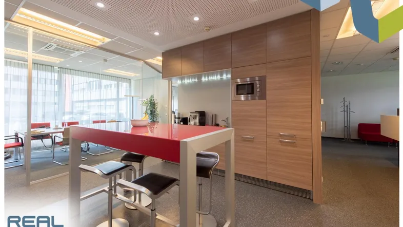 Moderne Büroküche mit rotem Tresen, Holzeinbauten und Mikrowelle, angrenzend an einen Besprechungsraum.