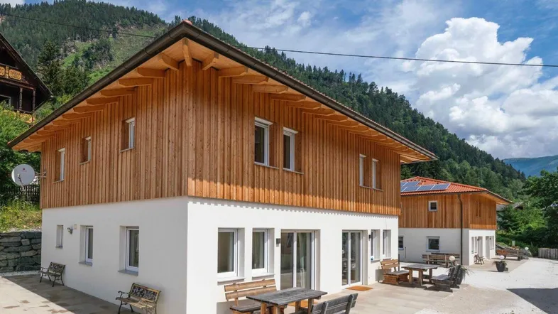 Modernes Haus mit Holzfassade und weißem Putz, umgeben von Bergen, mit gemütlicher Terrasse.