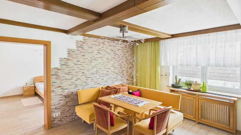 Gemütlicher Essbereich mit Holzbalken, Steinwandakzent und Blick in ein angrenzendes Schlafzimmer.