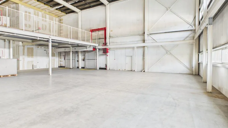 Geräumige Lagerhalle mit hoher Decke, Betonboden und einer Zwischenebene, ideal für industrielle Nutzung.