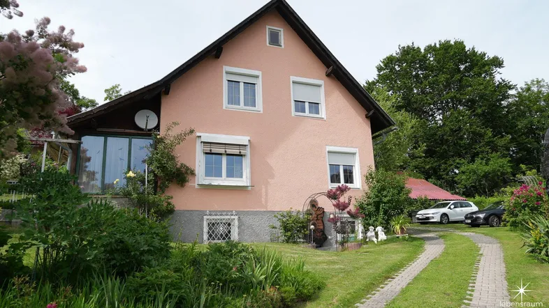 Rosa verputztes Einfamilienhaus mit Satteldach, Vorgarten und gepflasterter Auffahrt.