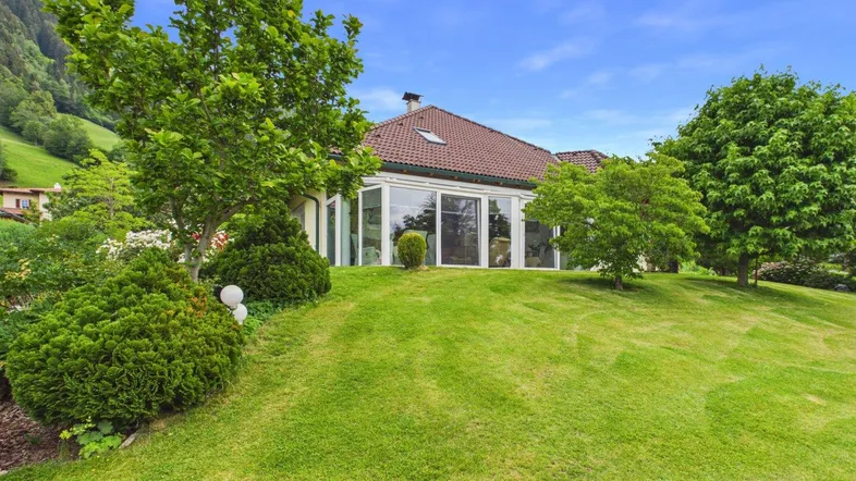 Großzügiger Gartenbereich mit gepflegtem Rasen und Blick auf das Haus mit Wintergarten.