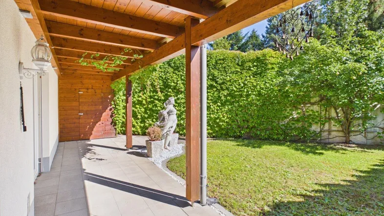 Überdachte Terrasse mit Holzbalken und Blick auf den gepflegten Gartenbereich.