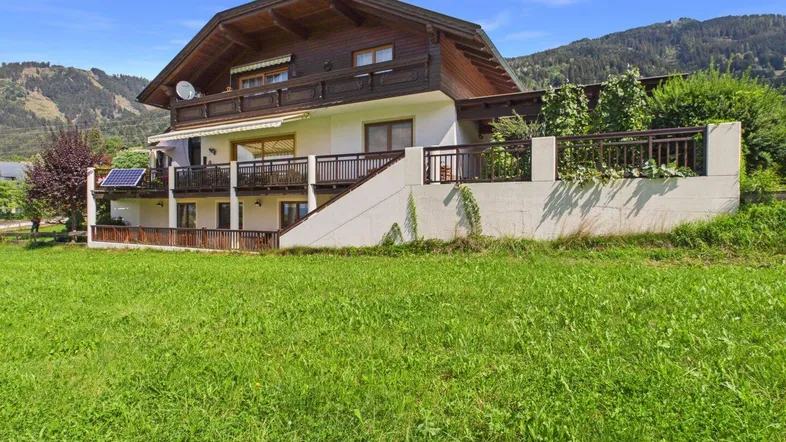 Traditionelles Haus im alpinen Stil mit Balkonen und Bergblick, umgeben von grünen Wiesen.