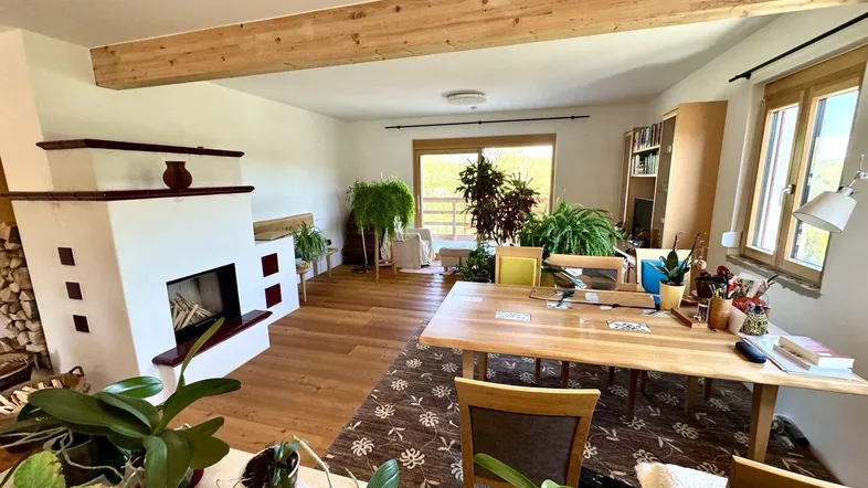 Helles Wohnzimmer mit Holzbalken, Kamin und Zugang zu einem Außenbereich mit viel Grün.
