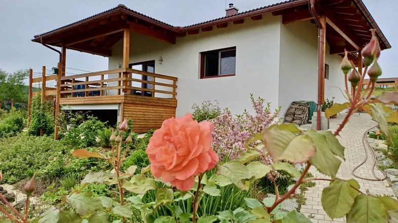 Charmantes Einfamilienhaus mit Holzterrasse und blühendem Rosengarten im Vordergrund.