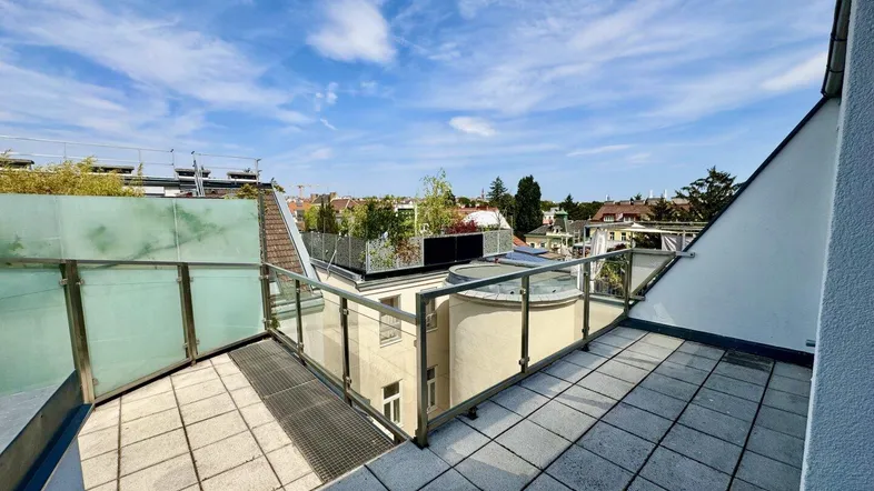 Geräumige Dachterrasse mit Fliesenboden und Glasgeländer, bietet einen weiten Blick über die Umgebung.