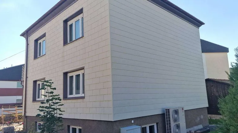 Modernes Wohnhaus mit heller Fassadenverkleidung und Wärmepumpe im Außenbereich.
