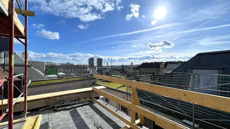 Panoramablick über die Stadt von einer Dachterrasse im Bau mit Gerüst und Sonnenschein.