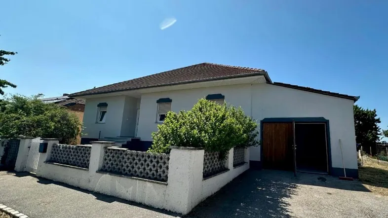 Einfamilienhaus mit weißer Fassade, braunem Dach und integrierter Garage unter blauem Himmel.
