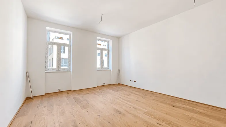 Helles, leeres Zimmer mit neuem Holzparkettboden und zwei Fenstern, bereit für die Einrichtung.