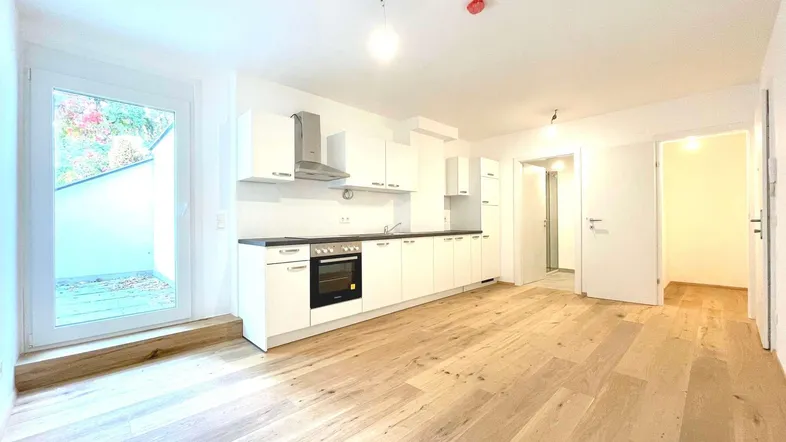 Moderne Einbauküche mit weißen Schränken und Holzfußboden, direktem Zugang zu einem Außenbereich.