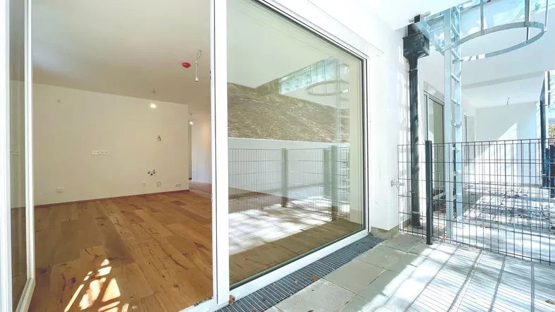 Helles Wohnzimmer mit Holzboden und großen Schiebetüren zu einer umzäunten Terrasse.