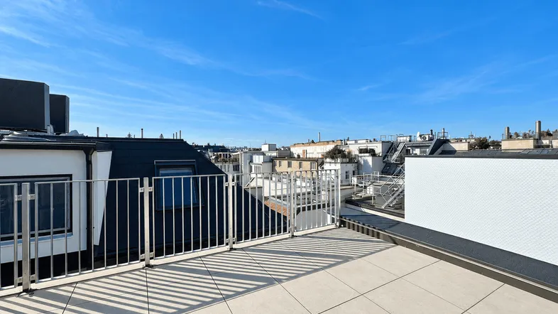 Geräumige Dachterrasse mit Fliesenboden und Blick über die umliegende Stadtlandschaft unter blauem Himmel.