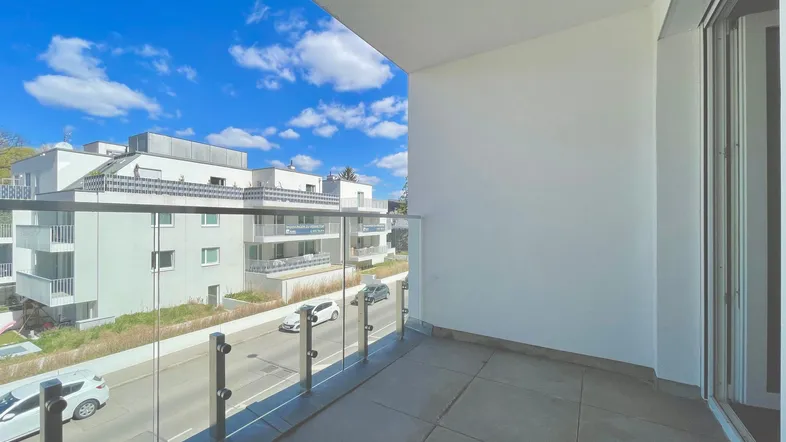 Moderner Balkon mit Glasbrüstung und Blick auf die Straße sowie umliegende Gebäude.