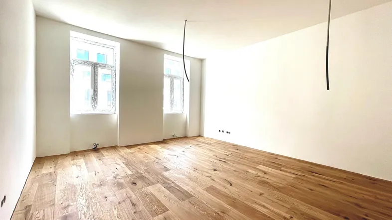 Helles, frisch renoviertes Zimmer mit neuem Holzboden und großen Fenstern, bereit zum Einzug.