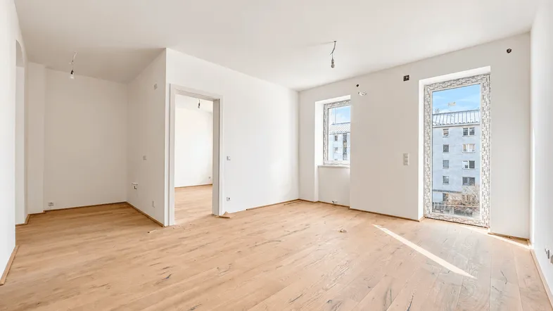 Heller, leerer Raum mit neuem Holzboden und Blick auf umliegende Gebäude.