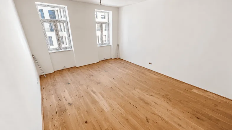 Helles, leeres Zimmer mit neuem Holzboden und zwei Fenstern, bereit zur individuellen Gestaltung.