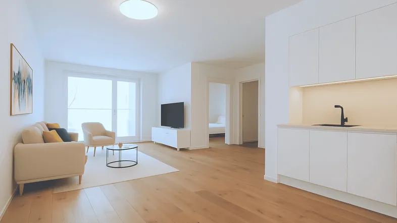 Helles, offenes Wohnzimmer mit integrierter Küchenzeile, Holzboden und Zugang zum Balkon.