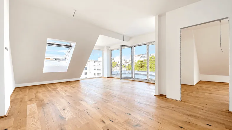 Helles, geräumiges Wohnzimmer mit Holzboden, Dachschrägen und Zugang zu einem Balkon.
