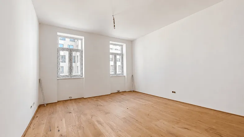 Helles, leeres Zimmer mit neuem Holzboden und zwei Fenstern, bereit für die Einrichtung.