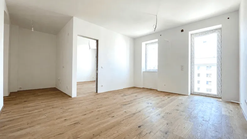 Helles, leeres Zimmer mit neuem Holzfußboden und großen Fenstern, bereit für die individuelle Gestaltung.