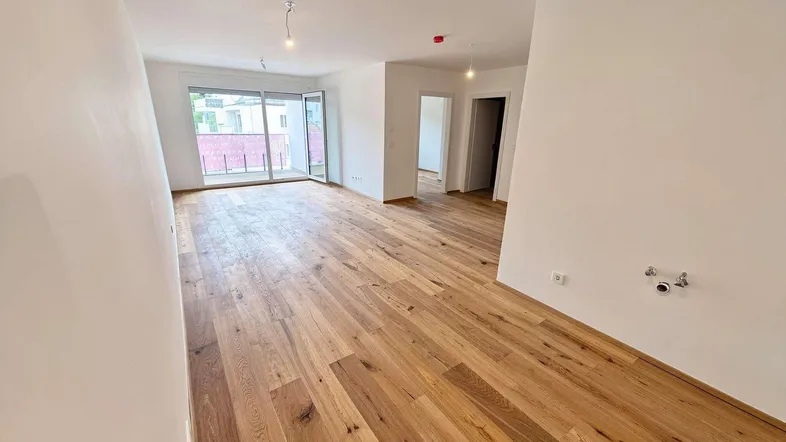 Geräumiges, helles Wohnzimmer mit neuem Holzboden und Zugang zu einem Balkon.