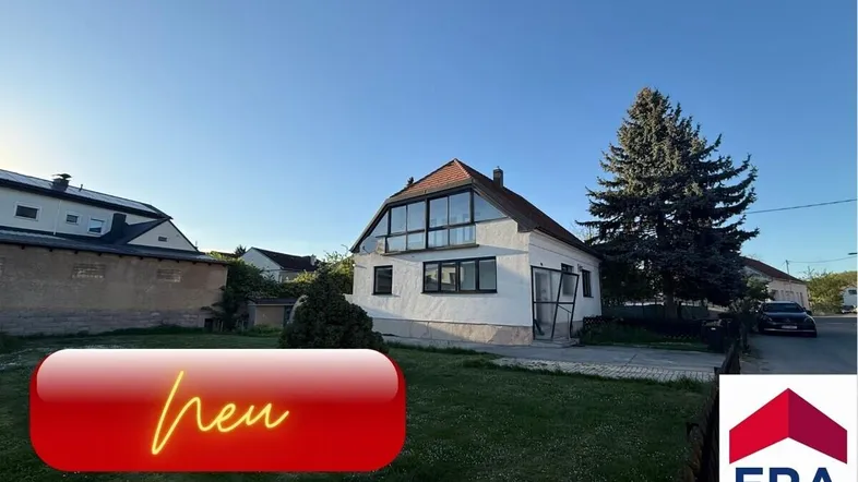 Freistehendes Einfamilienhaus mit großen Fenstern, Garten und altem Baumbestand unter blauem Himmel.