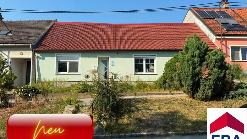 Einfamilienhaus mit rotem Ziegeldach und hellgrüner Fassade, umgeben von einem kleinen Vorgarten.