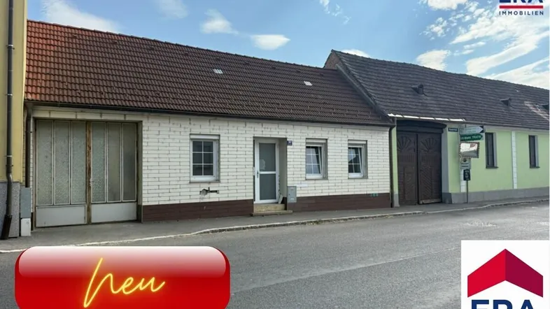 Vorderansicht eines Einfamilienhauses mit weißer Fassade und braunem Ziegeldach an einer Straße.