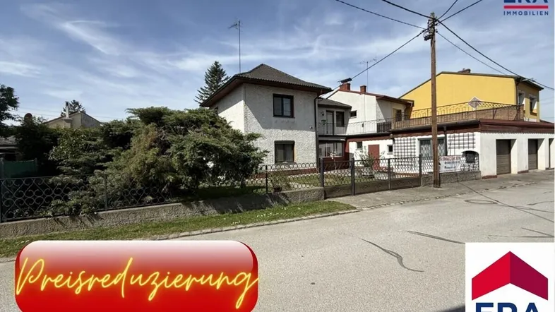 Ansicht des Hauses von der Straße mit Vorgarten und umliegenden Gebäuden unter bewölktem Himmel.