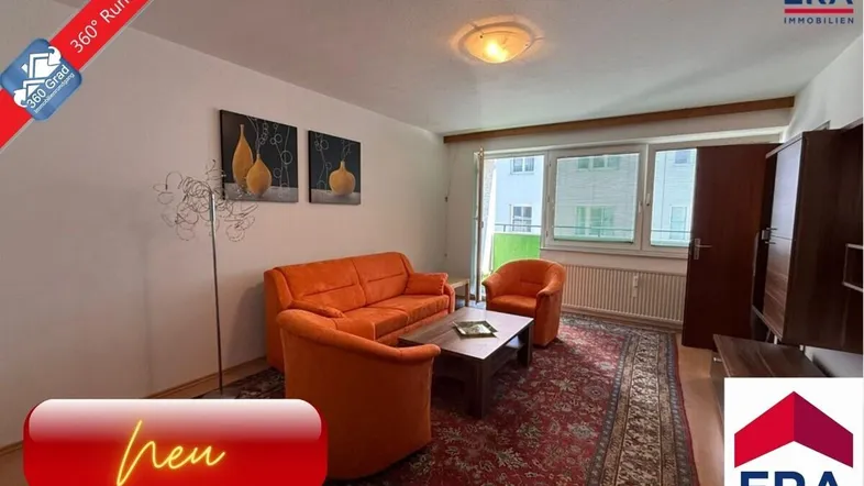 Gemütliches Wohnzimmer mit orangefarbenen Sofas, Teppichboden und Blick ins Grüne.