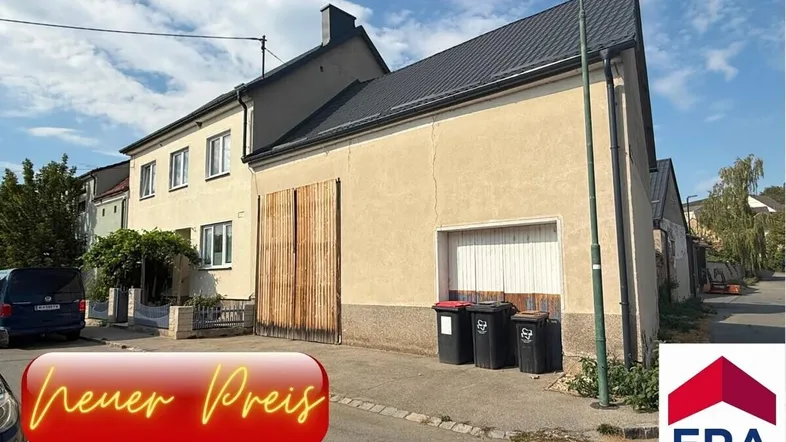 Gebäudeansicht von der Straße mit großem Holztor, Garagentor und einem Hinweis auf den neuen Preis.