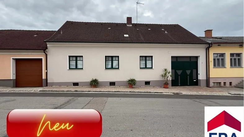Einfamilienhaus mit weißer Fassade und grünen Garagentoren an einer Wohnstraße.