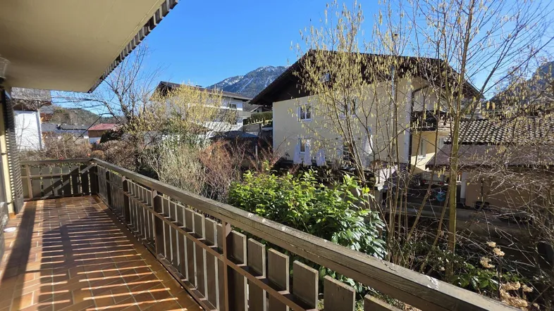 Sonniger Balkon mit traditionellem Holzgeländer und Blick auf die umliegende Berglandschaft.