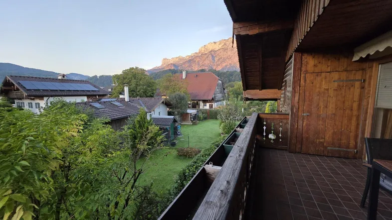 Geräumiger Holzbalkon mit Fliesenboden und weitem Blick auf die Berge, Gärten und umliegende Häuser.