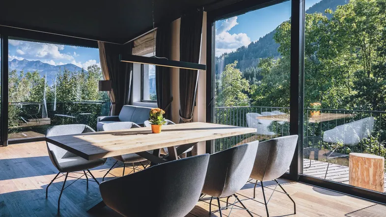 Heller Essbereich mit Holztisch, modernen Stühlen und raumhohen Fenstern mit Bergblick.