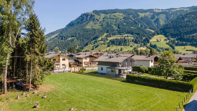 Panoramablick auf eine Wohnsiedlung mit gepflegten Häusern, umgeben von grünen Wiesen und majestätischen Bergen.