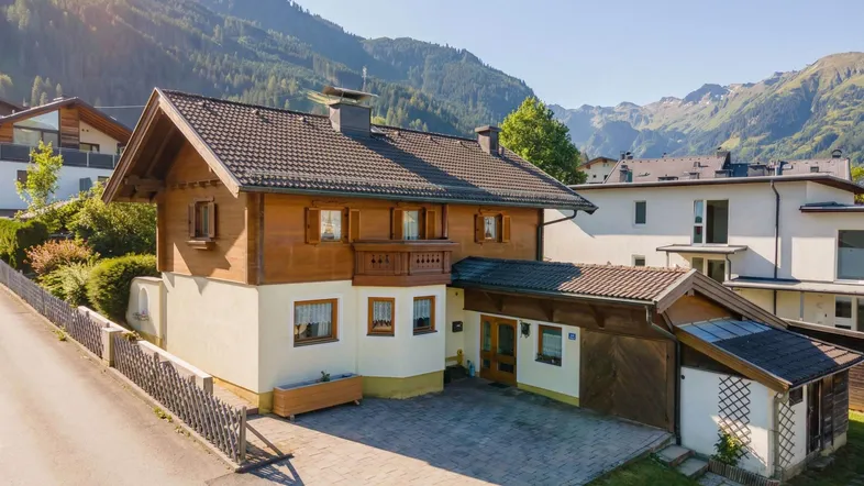 Traditionelles Haus mit Holzfassade und gepflasterter Einfahrt, umgeben von einer beeindruckenden Berglandschaft.