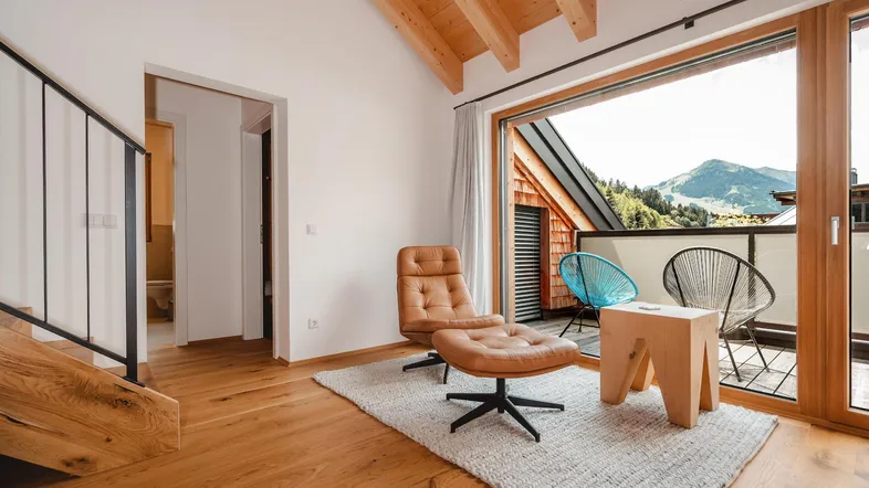 Helles Wohnzimmer mit Holzbalkendecke, Parkettboden und Zugang zu einem Balkon mit Bergblick.