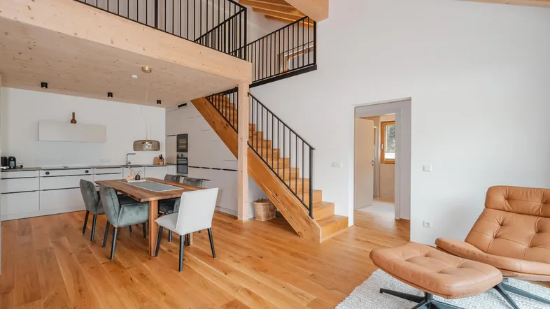Helles, offenes Wohn- und Esszimmer mit integrierter Küche, Holztreppe und sichtbaren Holzbalken.