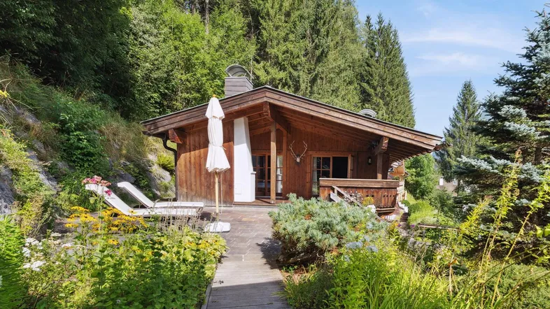 Charmantes Holzchalet in alpiner Umgebung mit üppigem Garten und Sonnenterrasse, umgeben von Bäumen.