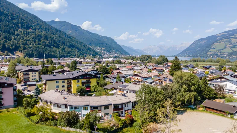 Panoramablick auf eine malerische Stadt am Seeufer, umgeben von majestätischen Bergen und grüner Landschaft.