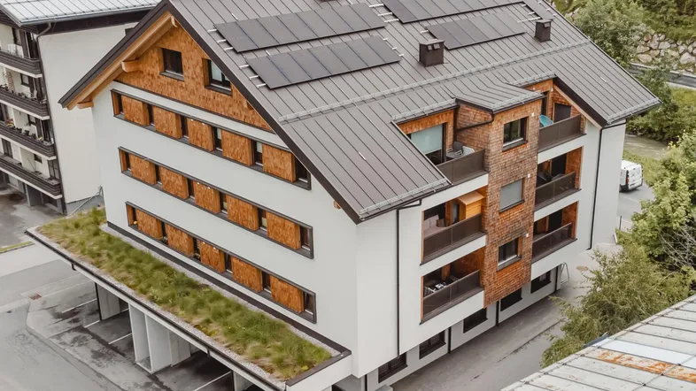 Modernes Apartmentgebäude mit Holzfassade, Balkonen, Solaranlage und begrüntem Carport.