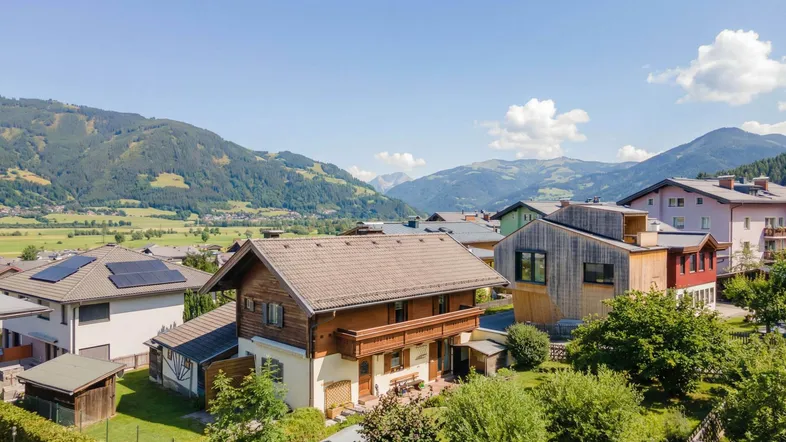 Luftaufnahme eines Hauses mit traditioneller Holzfassade und Ziegeldach in einer Berglandschaft.